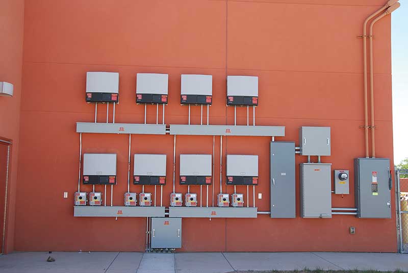 Photo 6. Eight PV systems with eight dc disconnects below eight utility-interactive inverters feeding an ac combining panel (right of center) and then to a single ac system disconnect on the far right. Courtesy of John Wiles